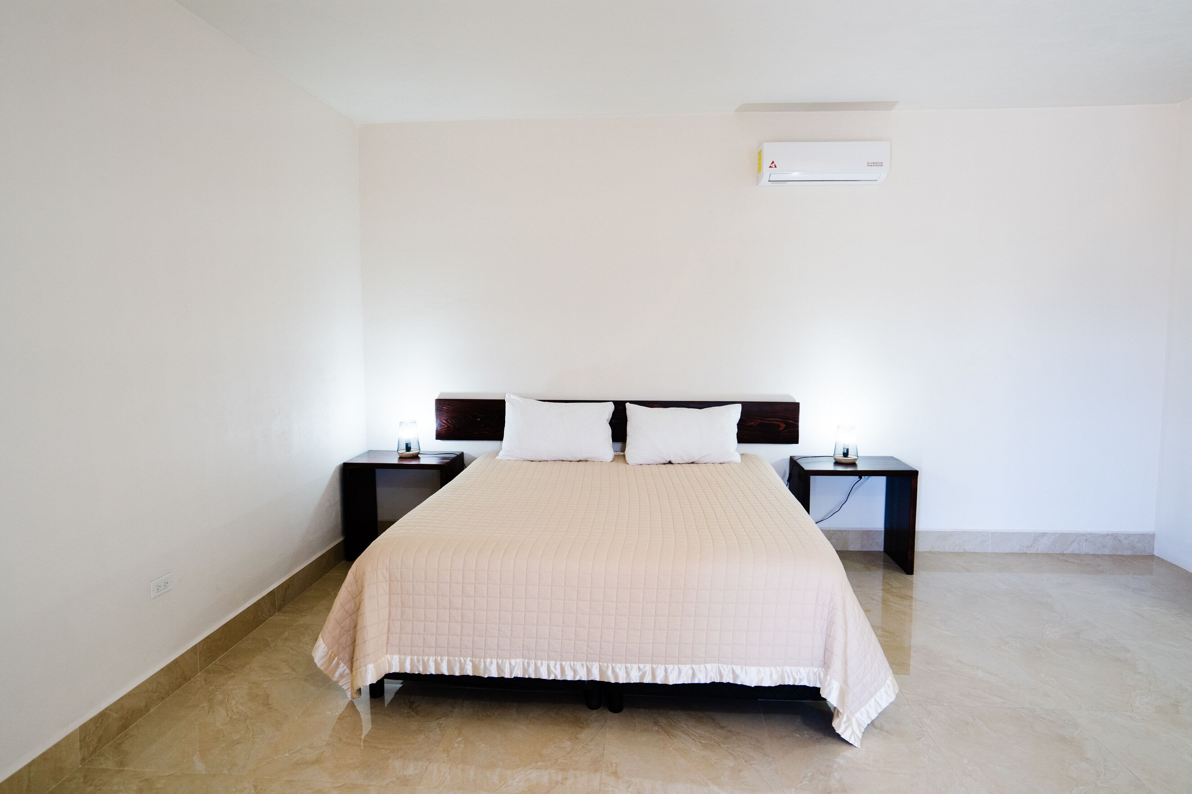 Un dormitorio con una cama, dos mesitas de noche y un equipo de aire acondicionado en la pared.