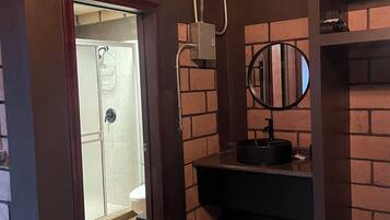 A bathroom with a brick wall, a wooden door, a sink with a mirror, and a shower area.