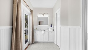A bathroom with a white vanity, a mirror with lights, and a shower area. - Hangloose Hideaway Beach House w/ a pool. 1 block to beach. Great fall rates! (Gulf Shores)