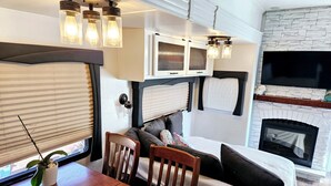 A cozy RV interior with a dining table, chairs, a sofa, and a fireplace.