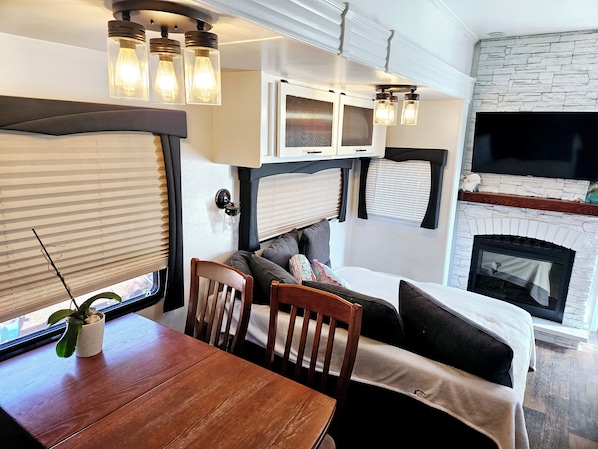 A cozy RV interior with a dining table, chairs, a sofa, and a fireplace.