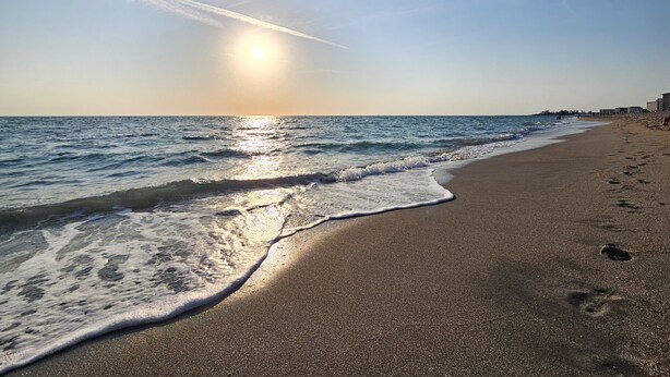 A beach with a clear sky and the sun setting or rising over the water.