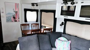 A compact RV interior with a bed, a dining area, and a kitchenette.