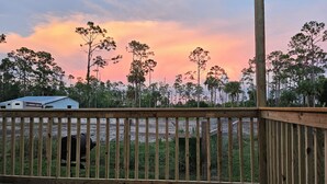 A wooden deck with a view of a grassy field and trees under a sunset sky.