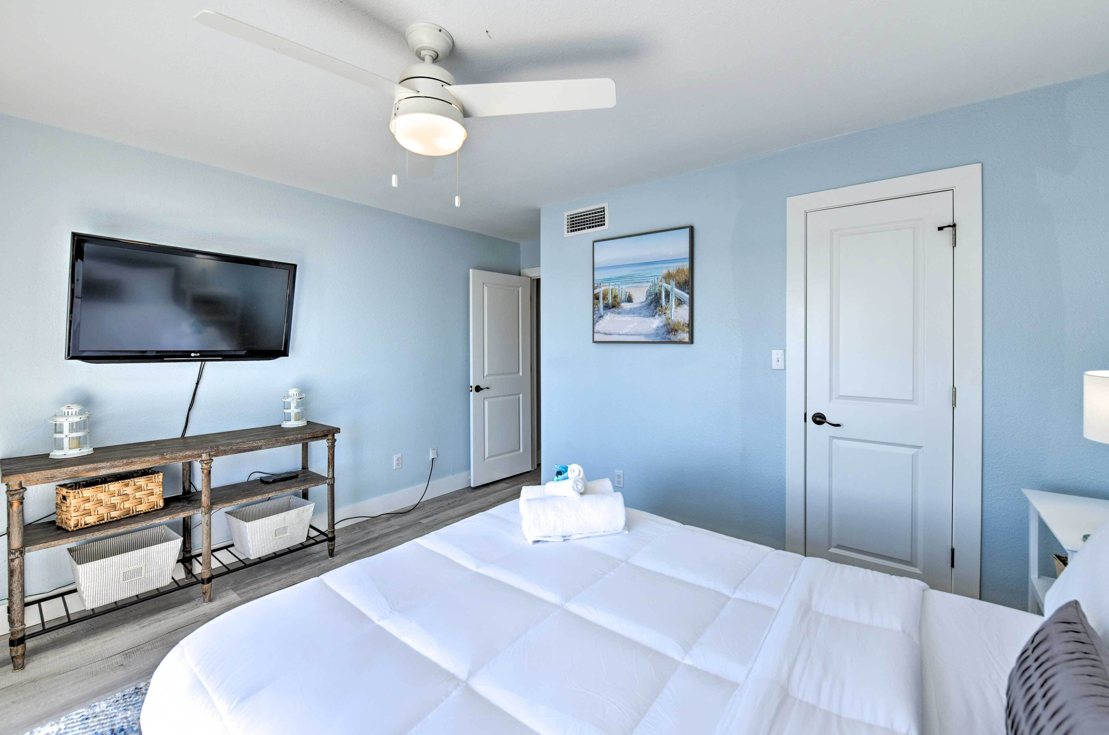 Une chambre à coucher avec un lit, un téléviseur, une table de chevet en bois et un ventilateur de plafond.