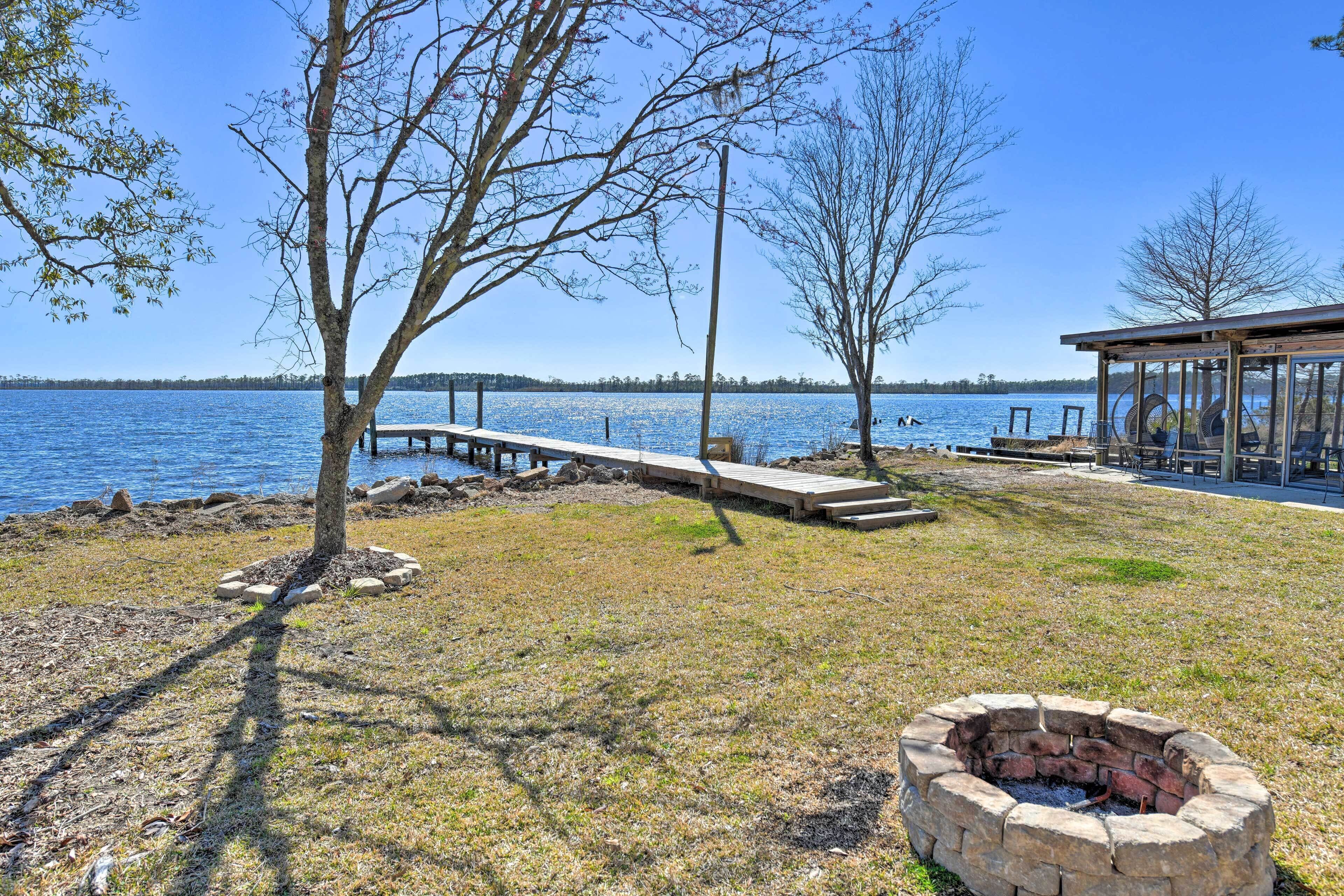 A lakeside property with a wooden dock, a fire pit, and a covered seating area.