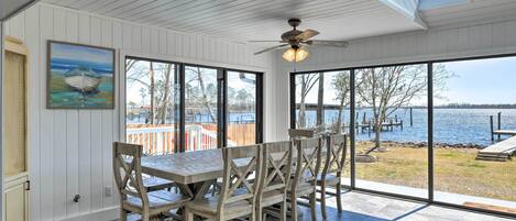 A dining area with a wooden table and chairs, large windows with a view of a lake, and a ceiling fan.