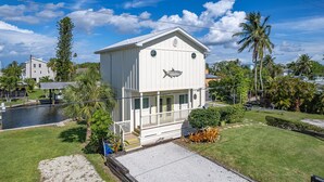 A white two-story building with a balcony, surrounded by palm trees and a body of water. - 2/2 Home in Bokeelia, Boat Lift Included! (Bokeelia)