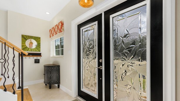 A hallway with a black-framed door with intricate glass designs, a wooden staircase, and a small cabinet. - 2/2 Home in Bokeelia, Boat Lift Included! (Bokeelia)