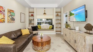 A modern living room with a brown leather sofa, a round wooden coffee table, and a television mounted on the wall. - 2/2 Home in Bokeelia, Boat Lift Included! (Bokeelia)