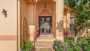 A building entrance with a double door, a wooden gate, and a small garden with pink flowers. - 3/2 Beautiful Pool Home on the Water in St. James City! (Saint James City)