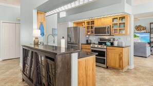 A modern kitchen with a central island, wooden cabinets, stainless steel appliances, and a view of the living area. - 3/2 Beautiful Pool Home on the Water in St. James City! (Saint James City)