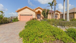 A two-story house with a garage, surrounded by lush greenery and palm trees. - 3/2 Beautiful Pool Home on the Water in St. James City! (Saint James City)