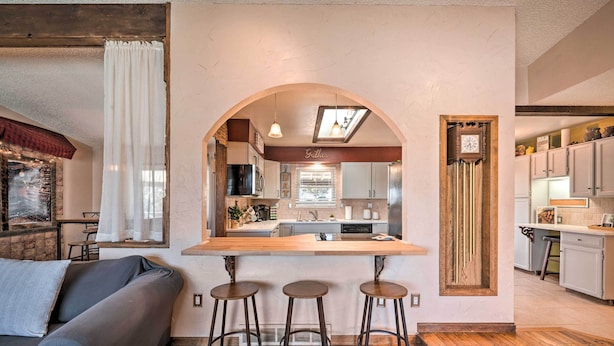 A modern kitchen with an archway leading to a dining area, wooden bar stools, and a sofa in a living room. - Arvada Home w/ Deck & Game Room Near Olde Town! (Arvada)