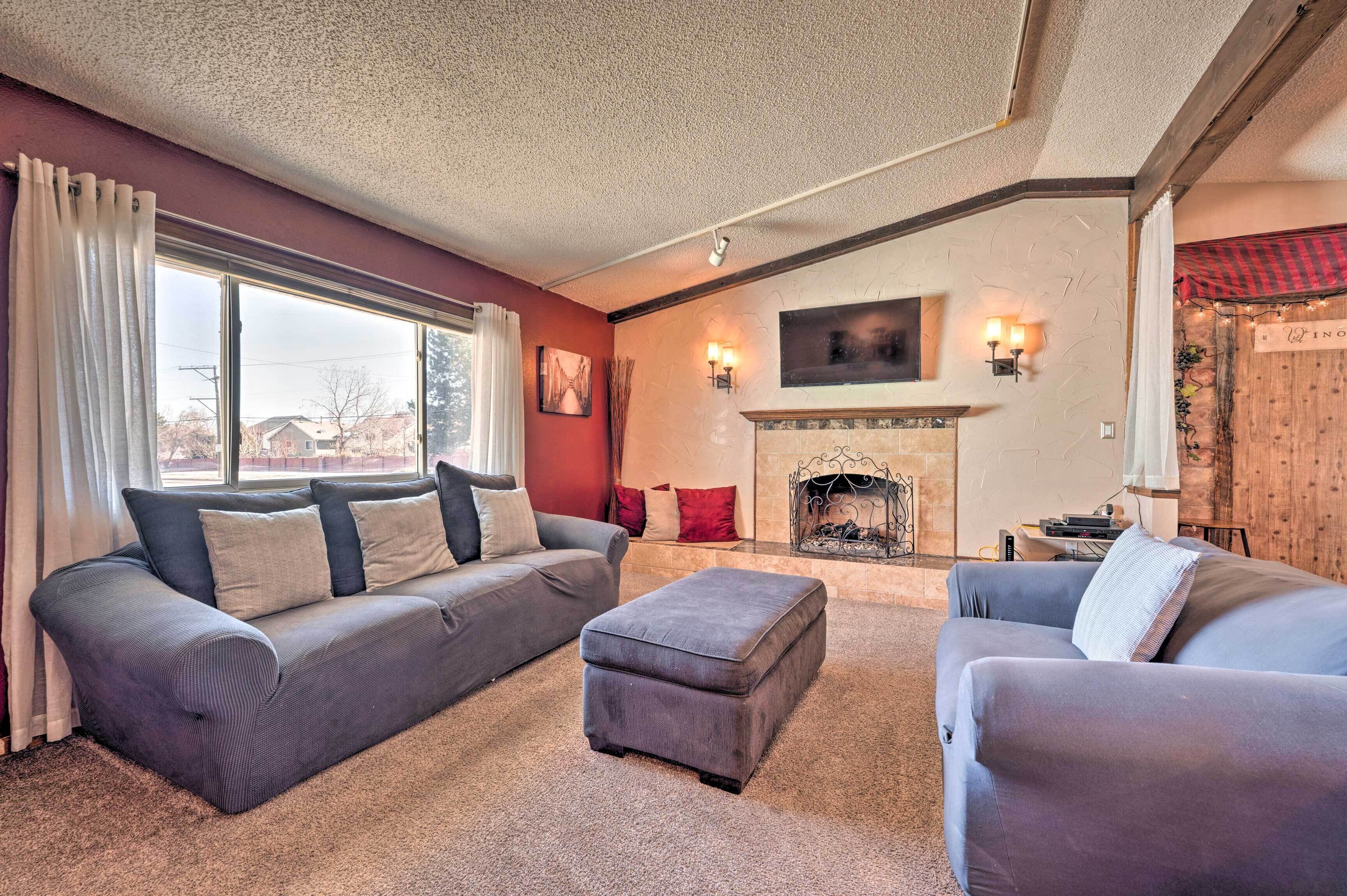 A living room with a fireplace, a sofa, an ottoman, and a window with curtains.