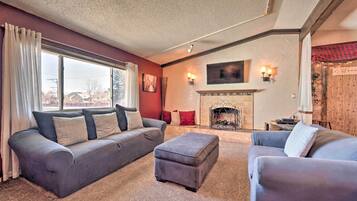 A living room with a fireplace, a sofa, an ottoman, and a window with curtains.
