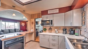 A compact kitchen with a built-in oven, microwave, and sink. It features light-colored cabinets, a wooden countertop, and a view into the living area. - Arvada Home w/ Deck & Game Room Near Olde Town! (Arvada)