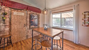 A rustic dining area with a wooden table and bar stools, a hanging light fixture, and a brick wall with a 'DINO' sign. - Arvada Home w/ Deck & Game Room Near Olde Town! (Arvada)