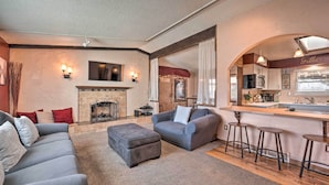 A living room with a fireplace, a sofa, an ottoman, and a kitchen area with a bar. - Arvada Home w/ Deck & Game Room Near Olde Town! (Arvada)