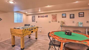 A room with a foosball table, a pool table, and a bar area.