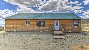 A wooden cabin with a green roof, a front porch, and a gravel driveway.
