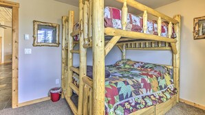 A bunk bed with a colorful quilt, wooden headboard, and a small red bucket on the floor.
