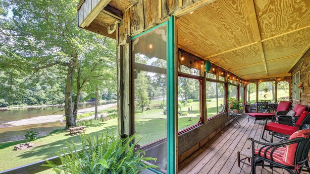 Une terrasse en bois avec des sièges extérieurs, offrant une vue sur une rivière et une zone verdoyante avec des arbres.