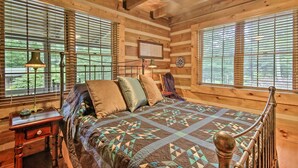 Un dormitorio tipo cabaña de madera con cama, paredes de madera y ventanas grandes.