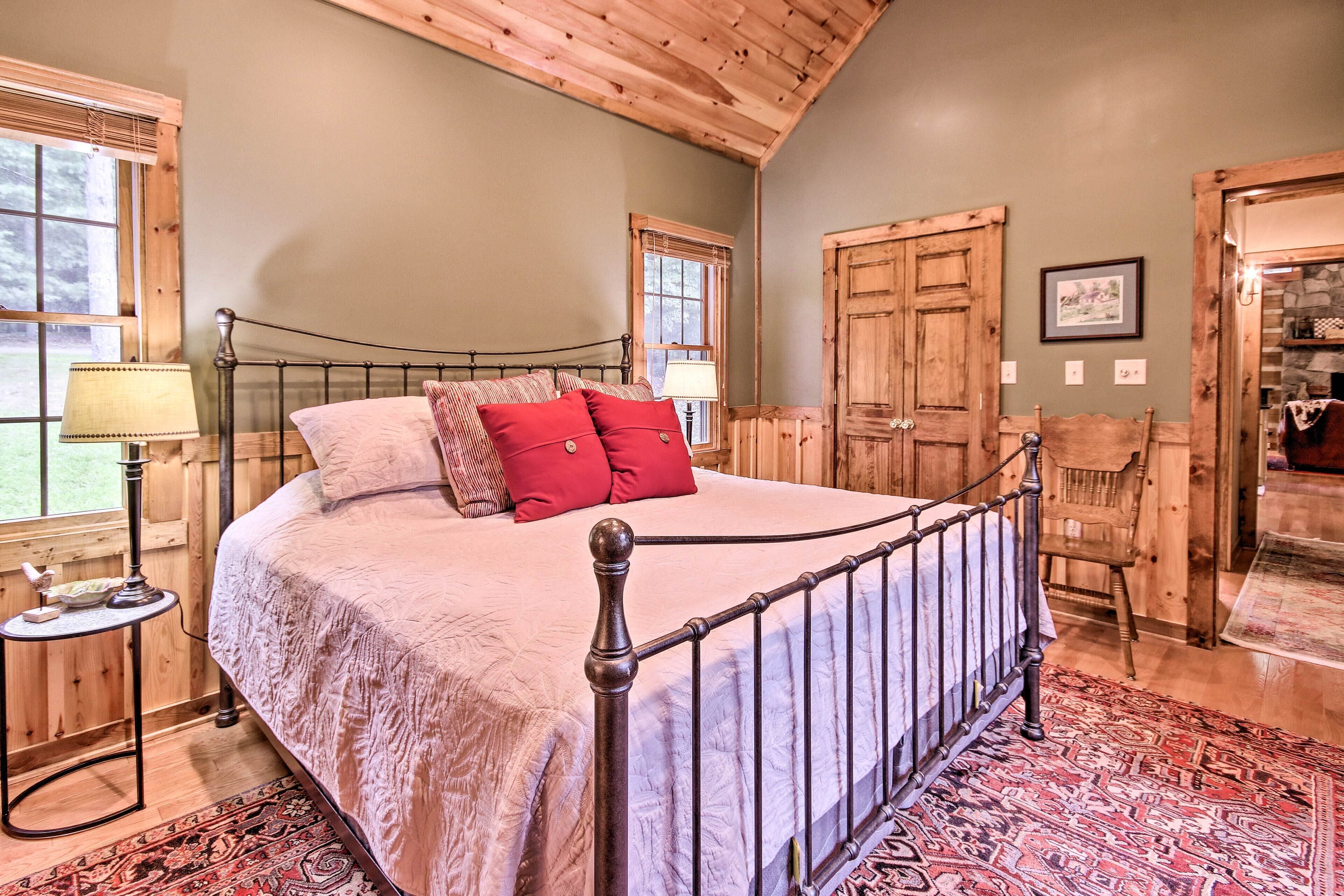 A bedroom with a wooden bed frame, a large window, and a door leading to another room.
