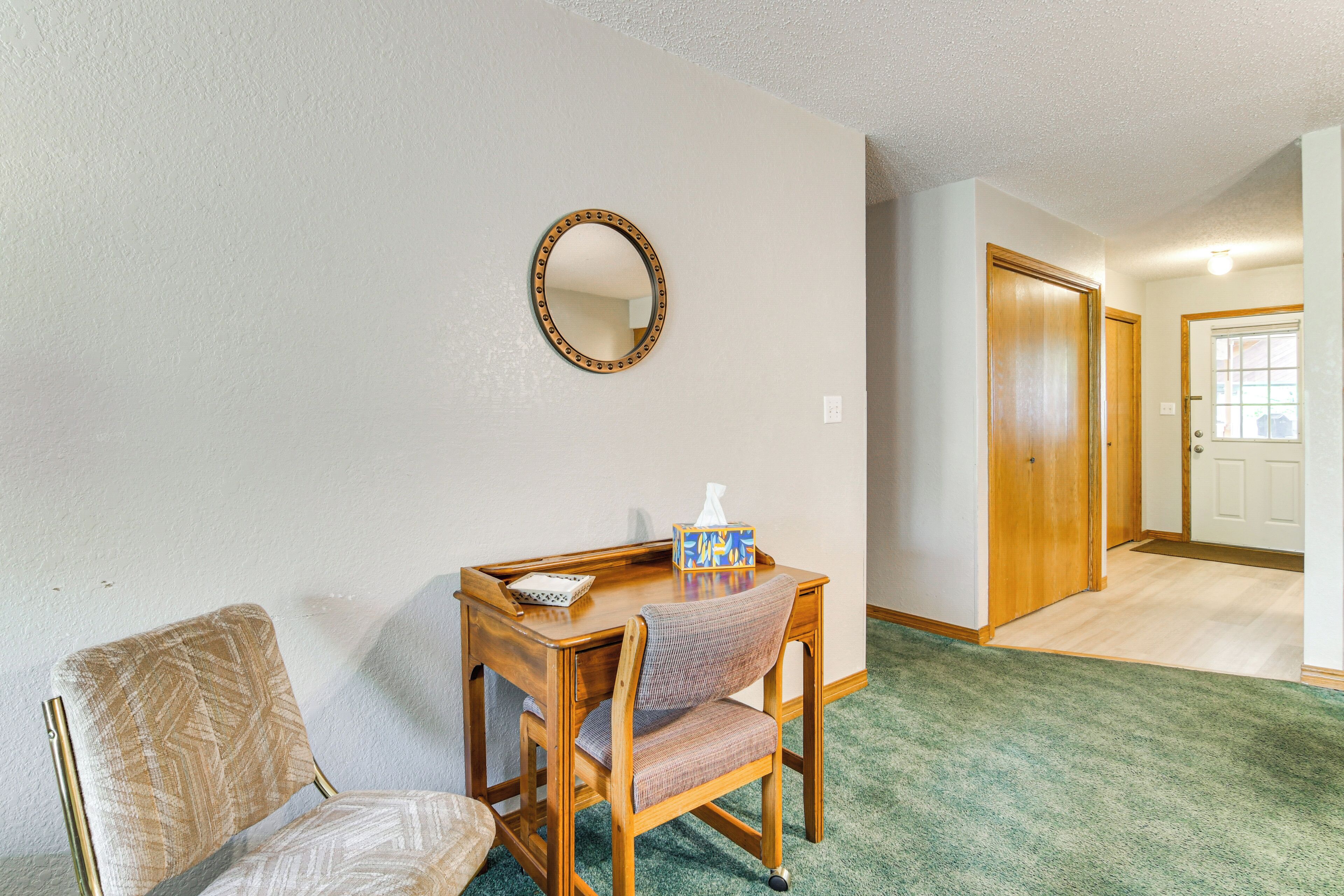 A room with a wooden desk, a chair, a mirror, and a carpeted floor.