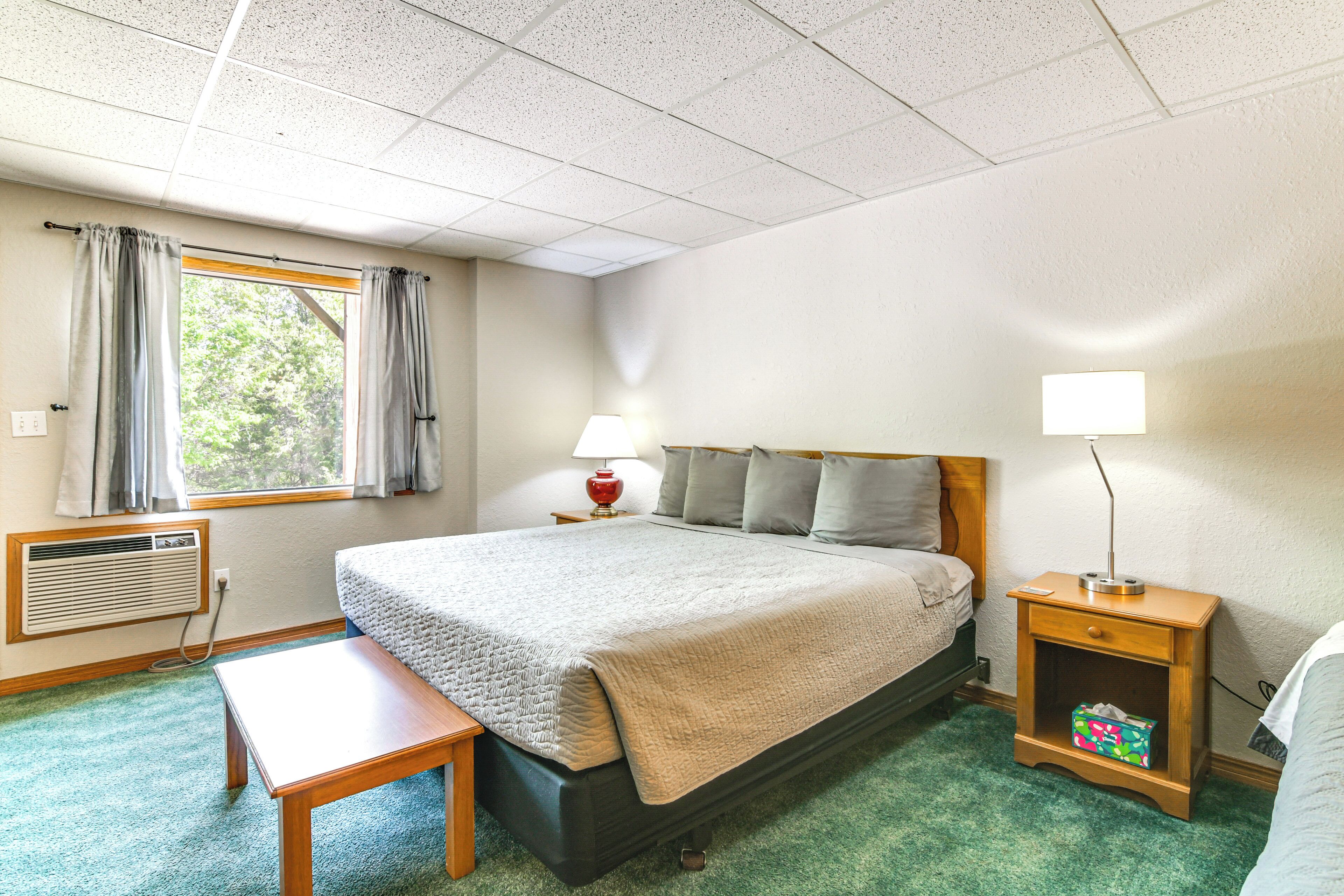 A hotel room with a bed, bedside table, lamp, nightstand, and a window with curtains.