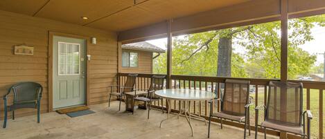 A covered porch with a table and chairs, a door, and a view of the outdoors.