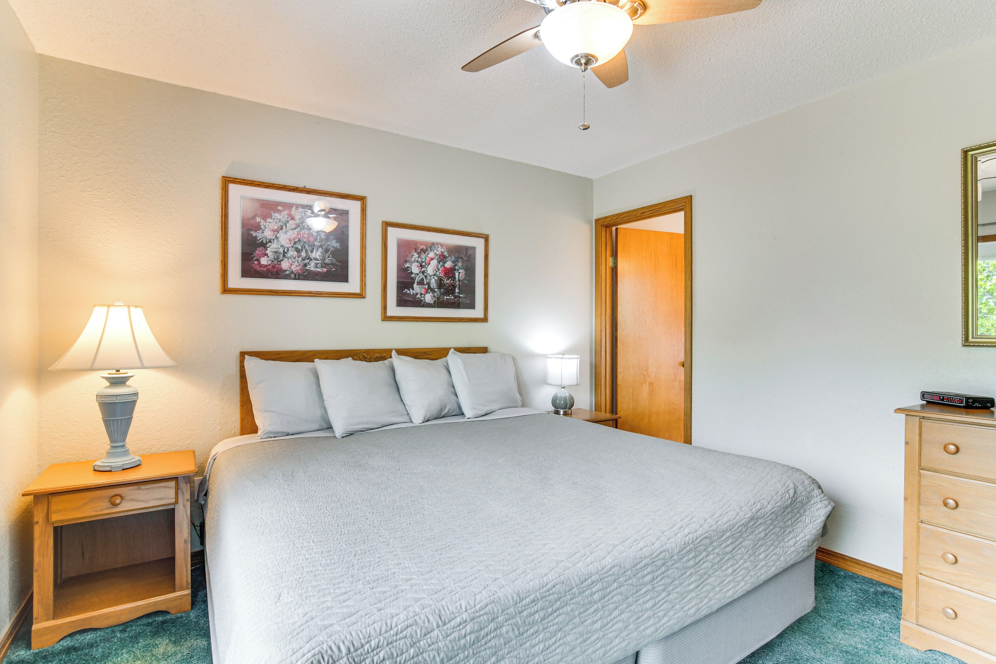 A bedroom with a bed, two wall-mounted lamps, a ceiling fan, and two framed floral paintings.