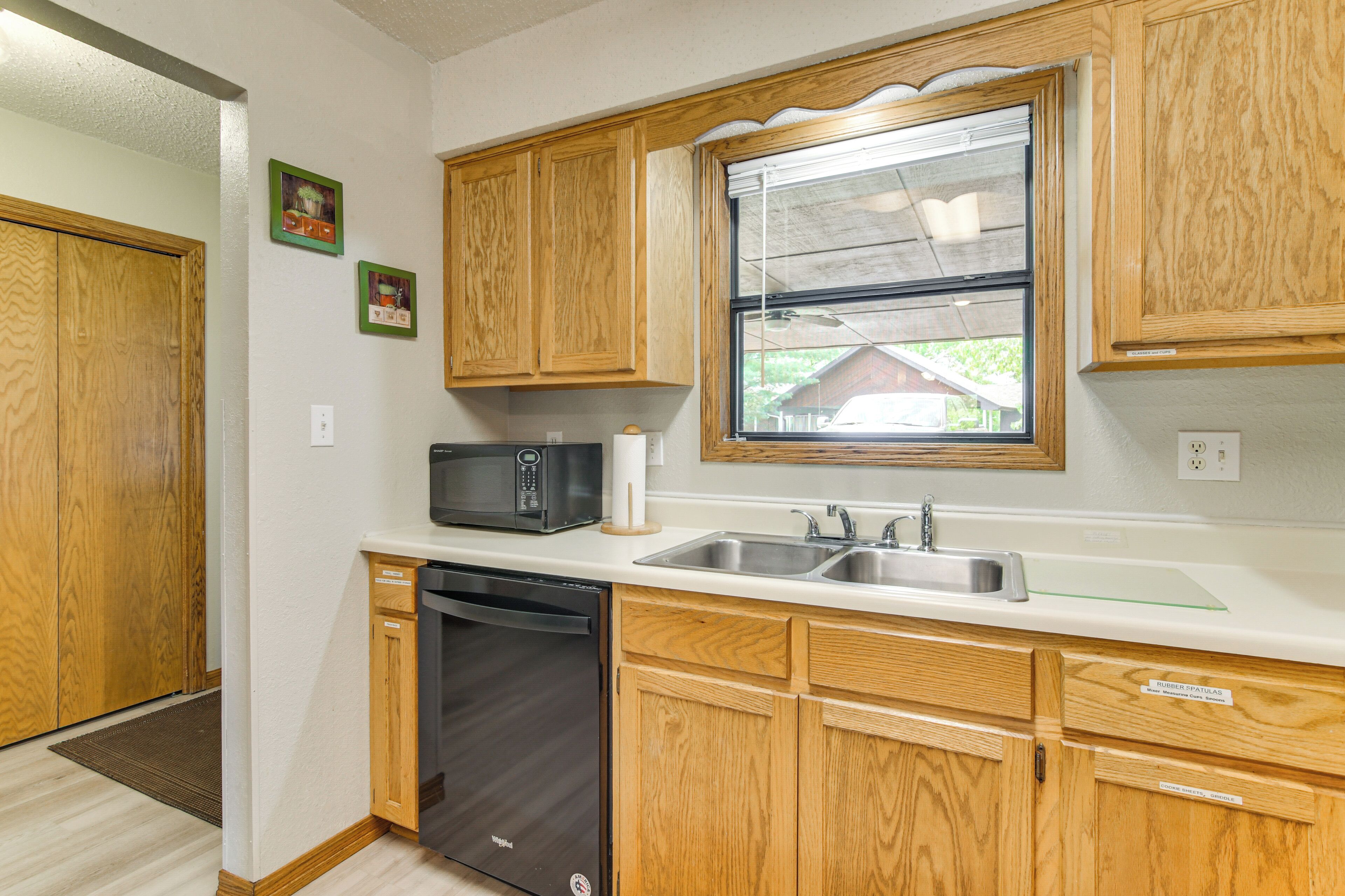 A kitchen with wooden cabinets, a dishwasher, a microwave, and a window above the sink.