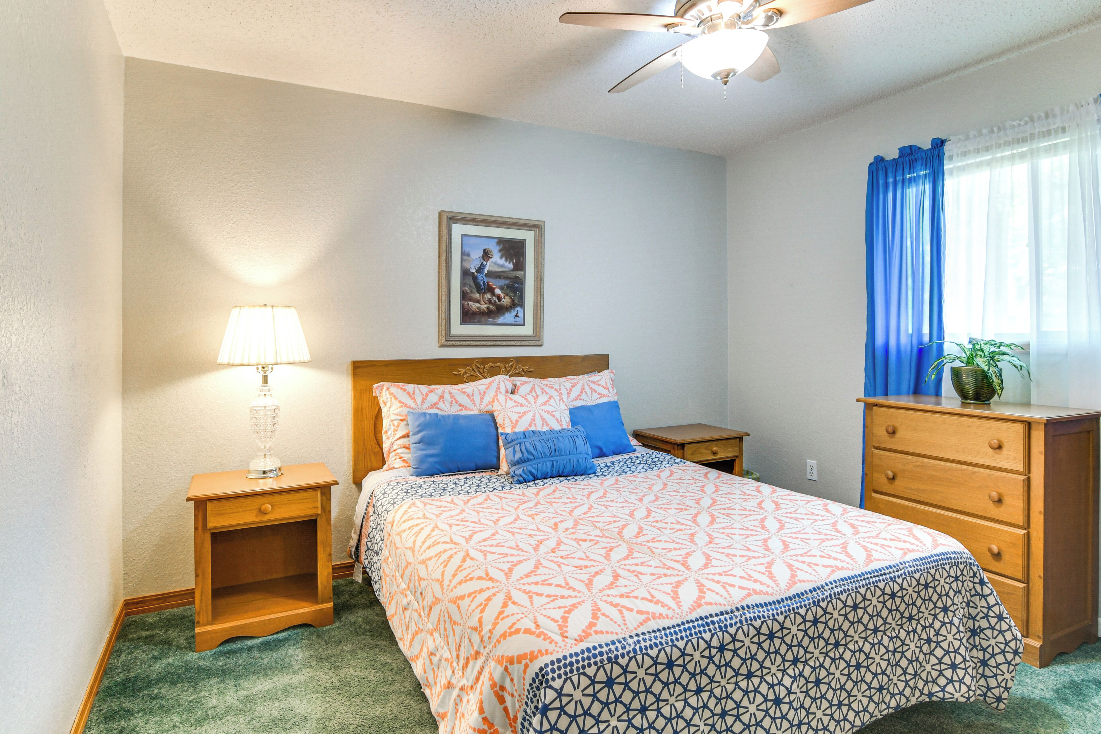 A bedroom with a bed, a nightstand, a dresser, a ceiling fan, a lamp, and a framed picture on the wall.