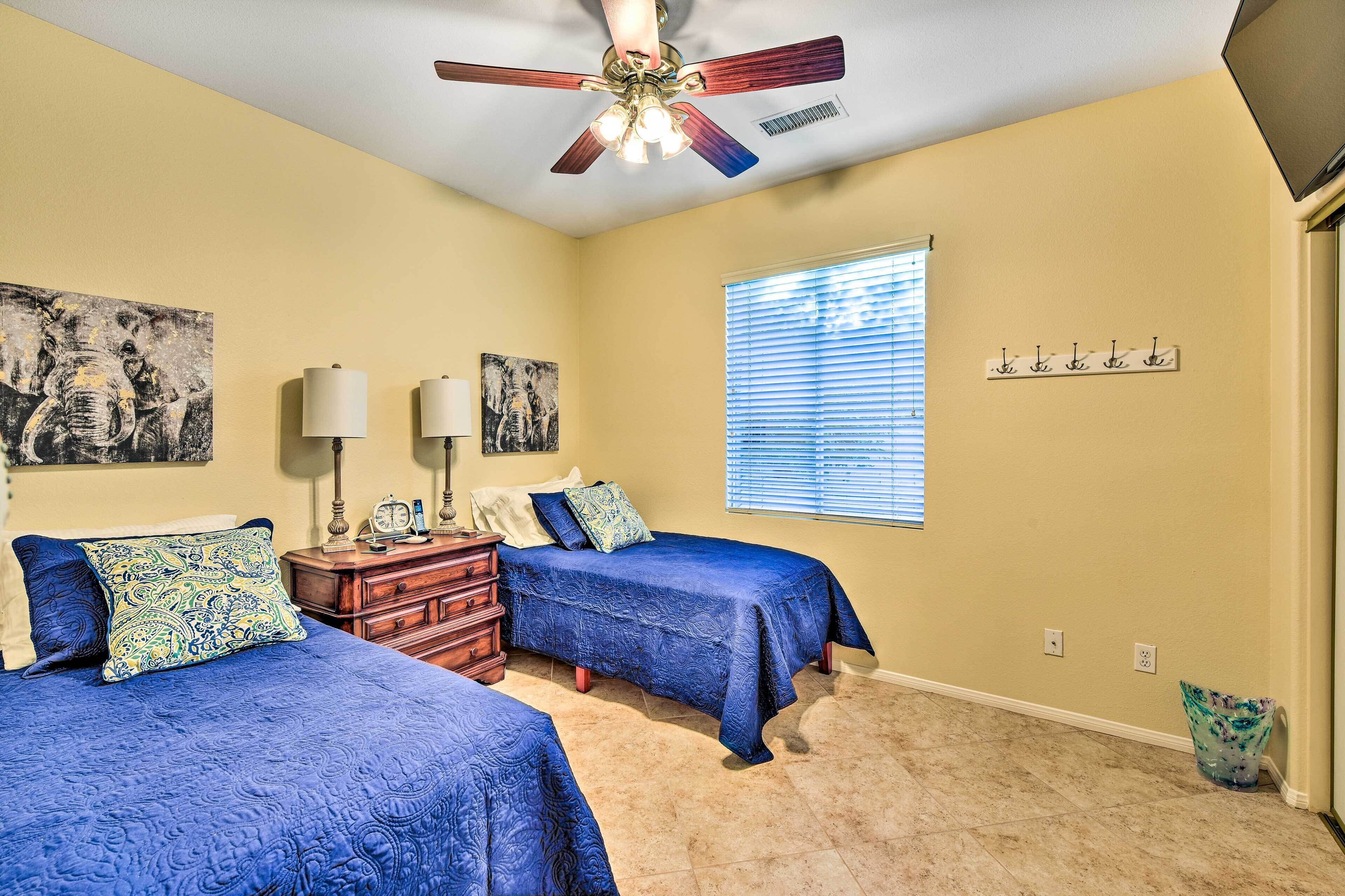 A bedroom with two beds, a ceiling fan, and artwork on the walls.