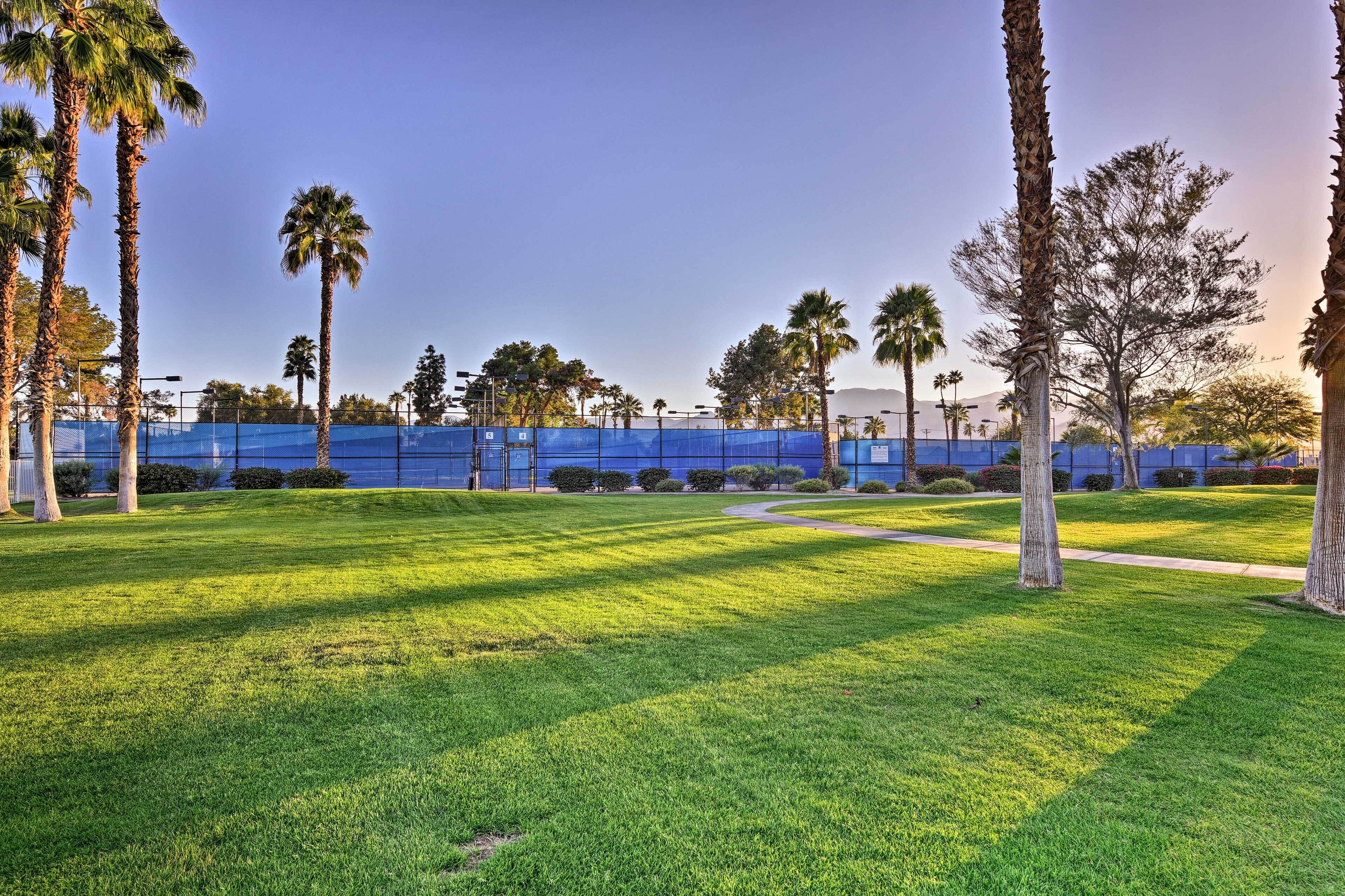 A well-maintained grassy area with palm trees, a blue fence, and a clear sky.