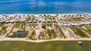 An aerial view of a coastal property with multiple buildings, a beach, and a large body of water. - Bayfront Dauphin Island Home w/ Beach Access! (Dauphin Island)