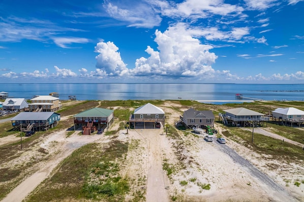 An aerial view of a coastal residential area with houses on stilts, a clear sky, and a calm sea. - Bayfront Dauphin Island Home w/ Beach Access! (Dauphin Island)