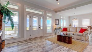 A spacious living room with a large window, a ceiling fan, and a cozy seating area. - Bayfront Dauphin Island Home w/ Beach Access! (Dauphin Island)