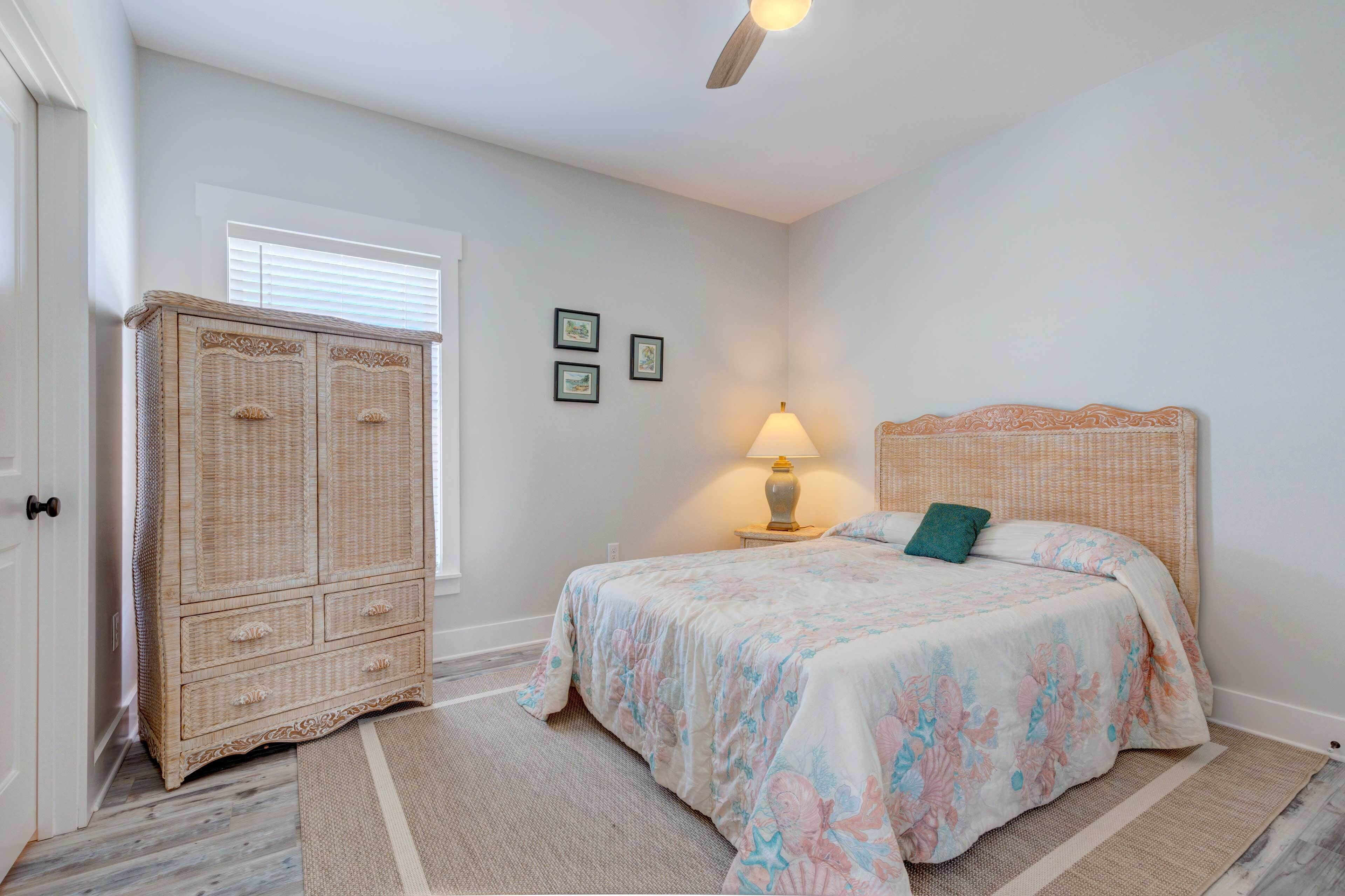 A bedroom with a bed, a nightstand, a lamp, a wicker wardrobe, and a window with blinds.
