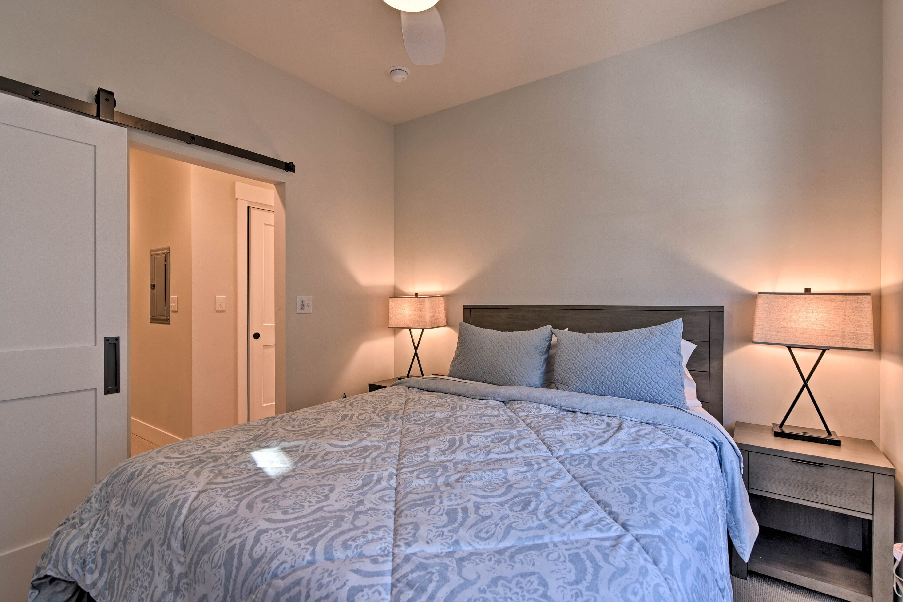 Une chambre à coucher avec un lit, deux tables de chevet avec des lampes, une porte et un ventilateur de plafond.