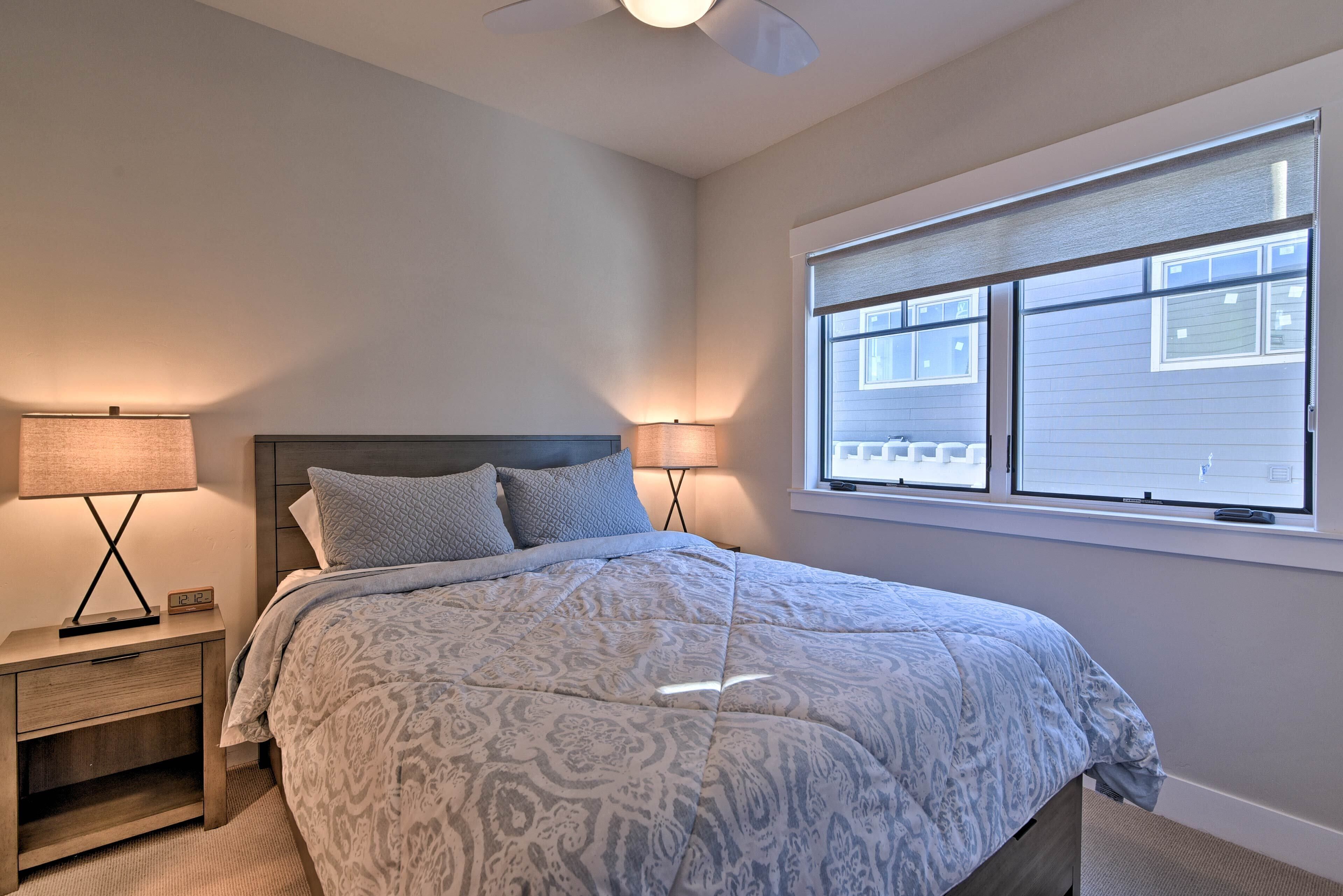 Une chambre à coucher comprenant un lit, des tables de chevet, des lampes, une fenêtre avec des stores et un ventilateur de plafond.