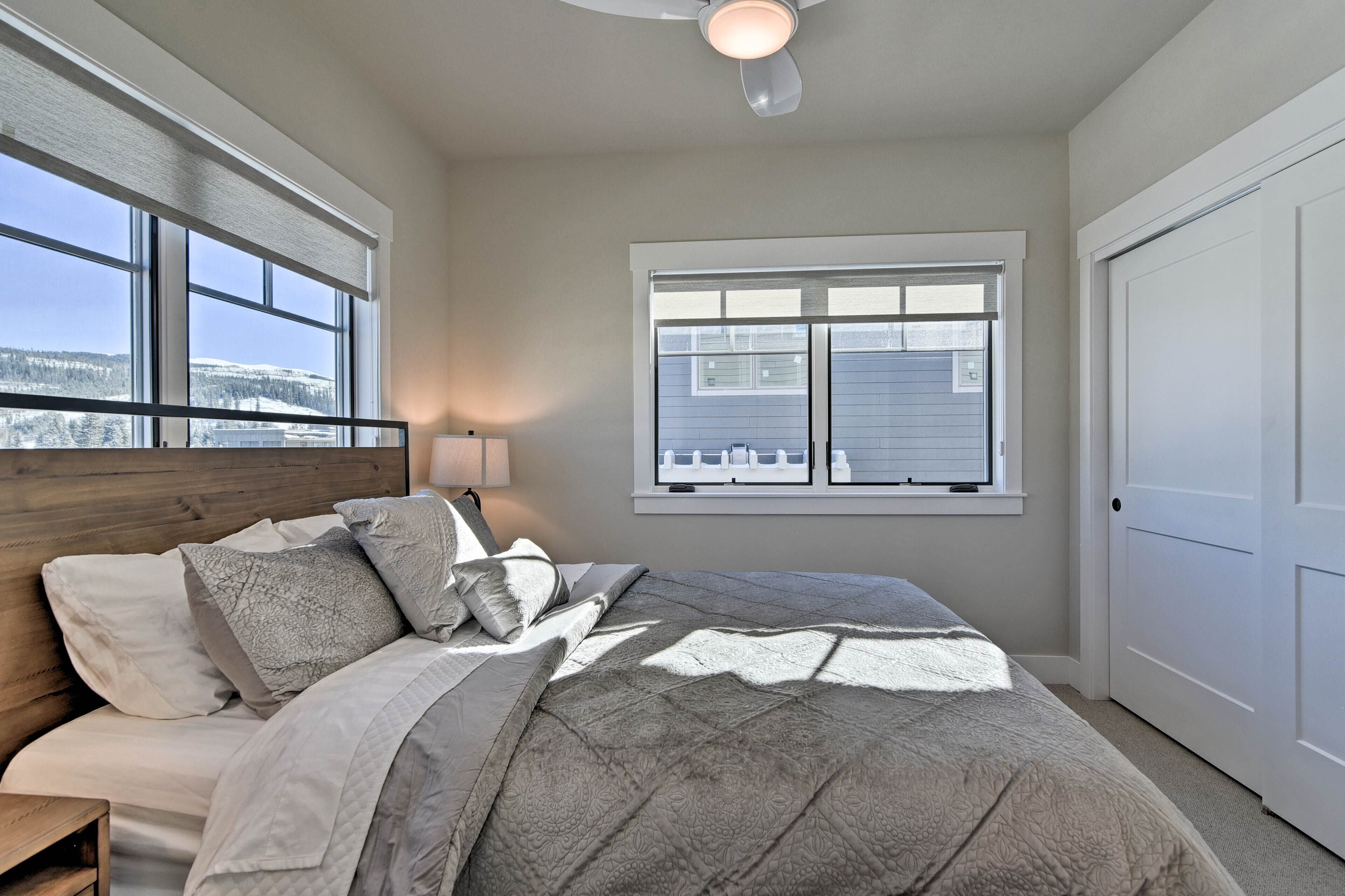A bedroom with a large bed, two windows, a ceiling fan, and a view of a snowy landscape.