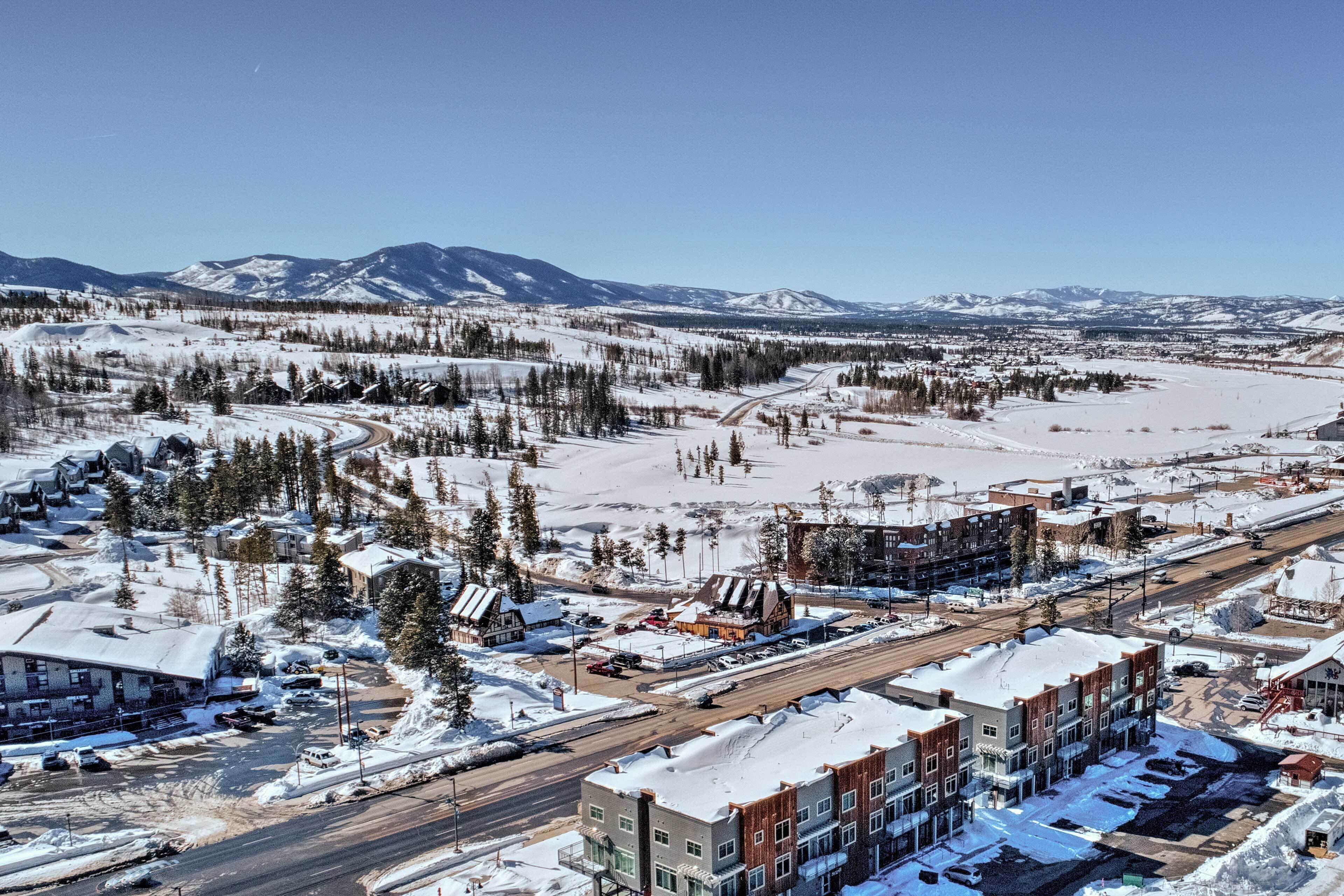 Un pueblo cubierto de nieve con edificios, caminos y montañas al fondo.