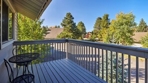 Une terrasse en bois avec une table et des chaises en métal, donnant sur un quartier résidentiel bordé d’arbres et de maisons.