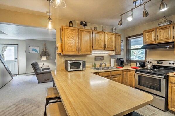 A modern kitchen with wooden cabinets, a central island, stainless steel appliances, and pendant lighting.