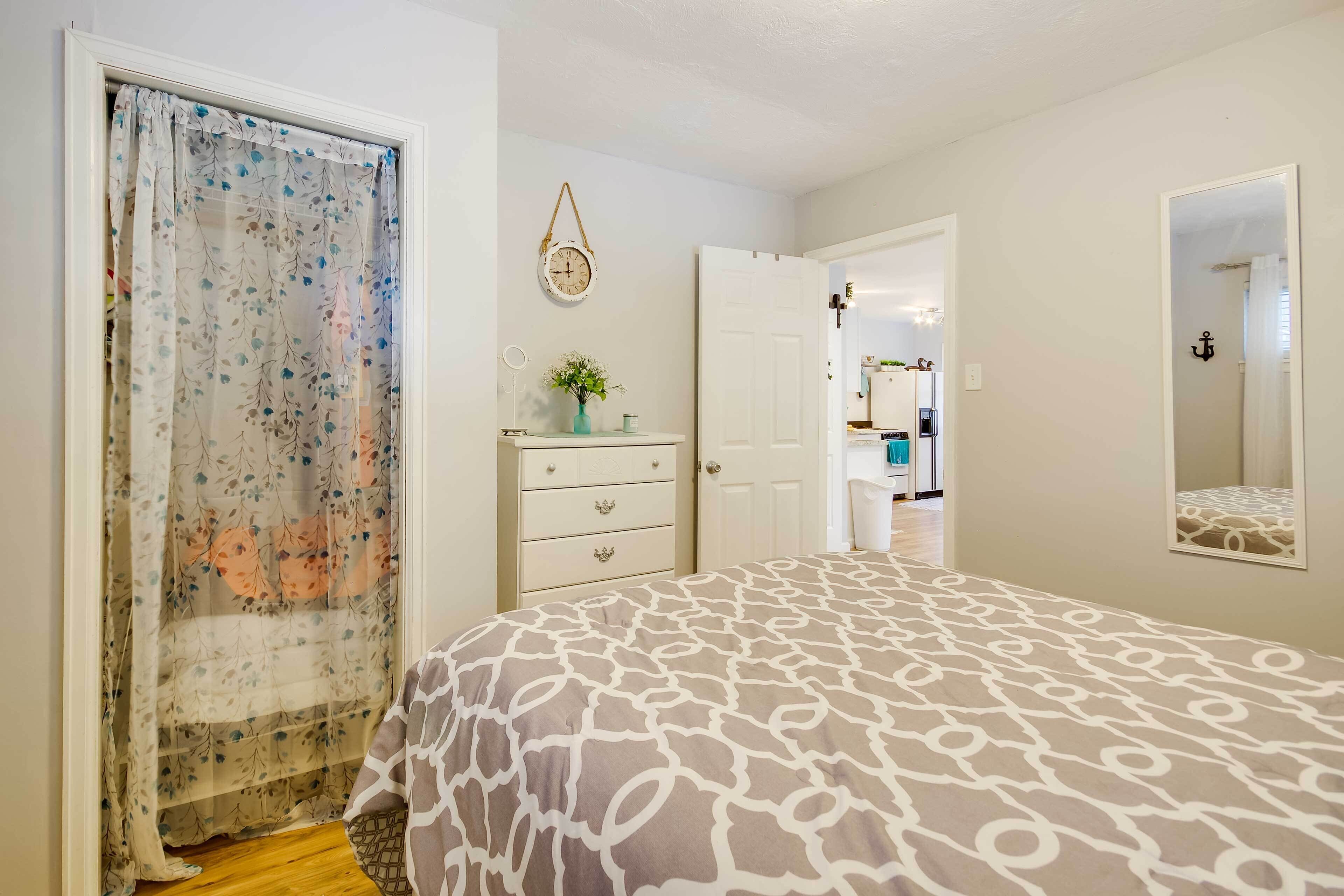 A bedroom with a bed, a dresser, a mirror, and a door leading to another room.