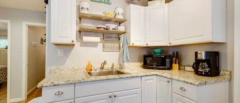 A kitchen with white cabinets, a granite countertop, a sink, a microwave, and a coffee maker.
