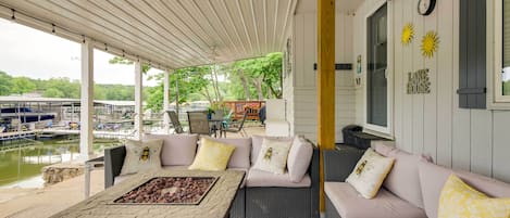 A covered outdoor seating area with a fire feature, cushioned sofas, and a view of a marina.